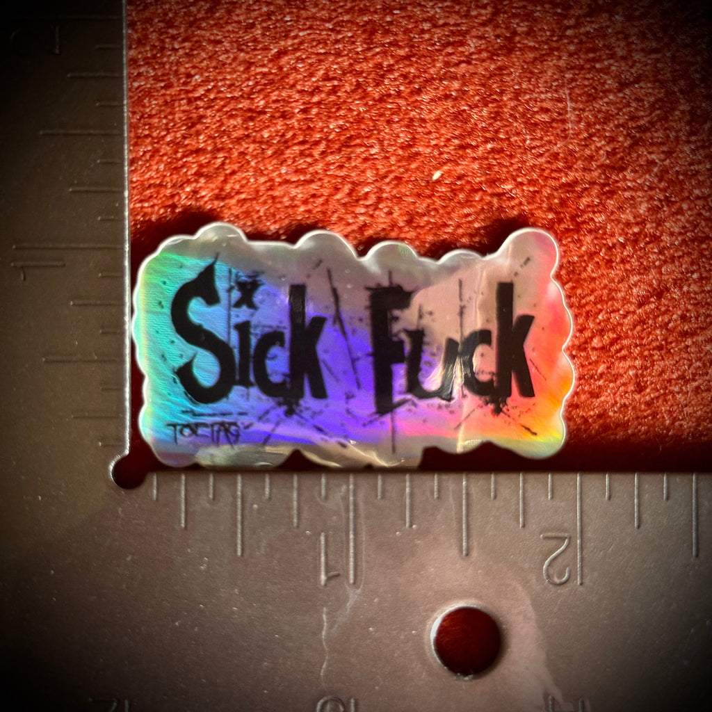 A small die-cut sticker with the words 'Sick Fuck' in black stylized lettering over holographic background, placed on a metal rulerfor scale.
